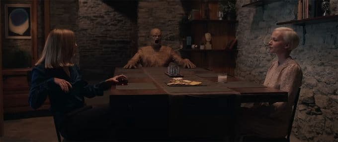 Two people and a life-sized wooden doll sit at a table.