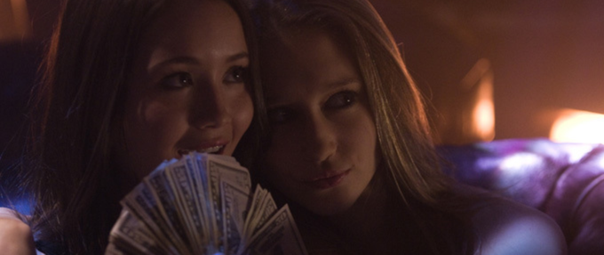 two girls holding up a fan of money looking mischevious