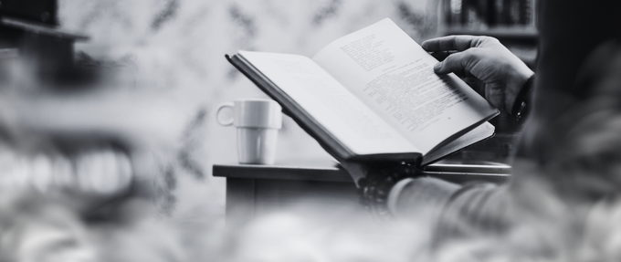 black and white photo of someone reading a book with a cup of coffee